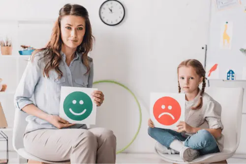Profissional e criança com cartões de emoção, representando regulação emocional infantil